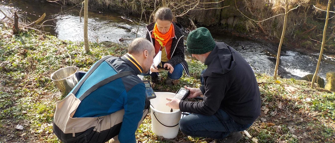 Drei Personen analysieren am Gewässer eine Wasserprobe