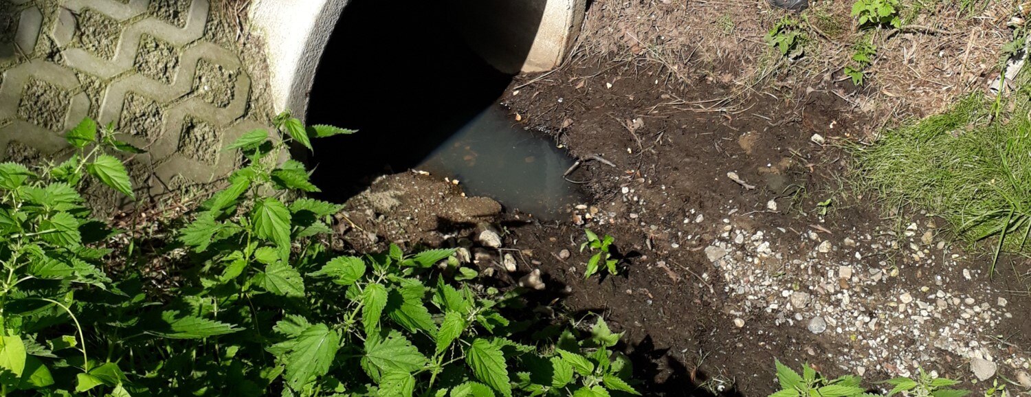 Bild: Trocken gefallener Strengebach bei Leipzig. Das Foto zeigt das Ende eines steinernen Rohres, wo sich eine kleine Wasserlache befindet. Das restliche Flussbett ist trocken gefallen, dort sind Erde und Kieselsteine zu sehen.